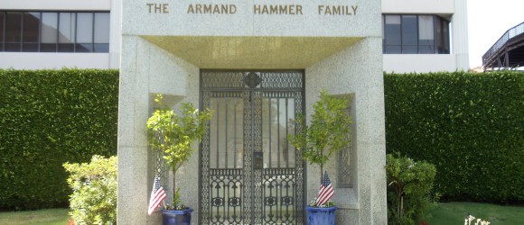 Granite mausoleum "The Armand Hammer Family," detailed craftsmanship by Forever Legacy; features potted plants with American flags, lush greenery backdrop.