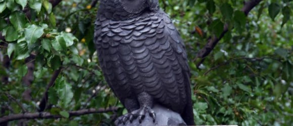 Bronze owl statue on stone pedestal amidst lush green foliage at Forever Legacy's custom private mausoleum grounds.